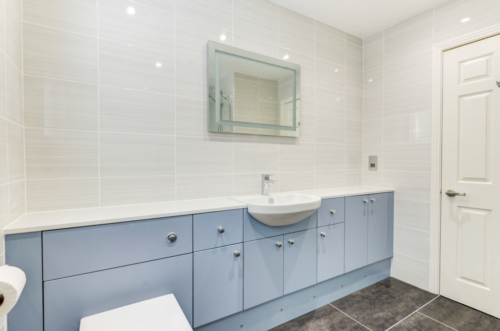 Inspiration för mellanstora moderna vitt badrum för barn, med släta luckor, blå skåp, ett badkar i en alkov, en dusch/badkar-kombination, en vägghängd toalettstol, beige kakel, keramikplattor, beige väggar, ett integrerad handfat, laminatbänkskiva och grått golv