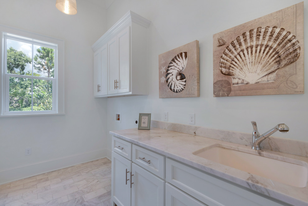 Photo of a mid-sized beach style single-wall utility room in Miami with an undermount sink, recessed-panel cabinets, white cabinets, marble benchtops, white walls, marble floors and a side-by-side washer and dryer.