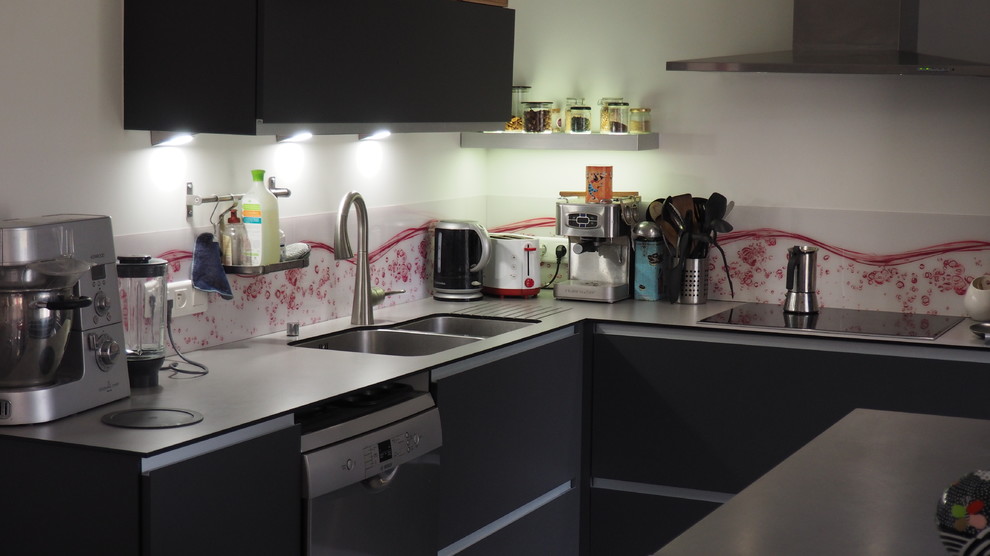 Small contemporary l-shaped open plan kitchen in Nantes with a double-bowl sink, flat-panel cabinets, grey cabinets, stainless steel benchtops, pink splashback, glass sheet splashback, stainless steel appliances, ceramic floors, with island and grey floor.