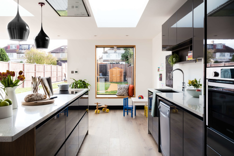 Design ideas for a contemporary galley kitchen in London with an undermount sink, flat-panel cabinets, black cabinets, white splashback, black appliances, light hardwood floors, with island, beige floor and white benchtop.