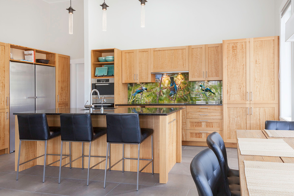 Photo of a mid-sized tropical eat-in kitchen in Auckland with a single-bowl sink, shaker cabinets, medium wood cabinets, granite benchtops, green splashback, glass sheet splashback, stainless steel appliances, ceramic floors and with island.