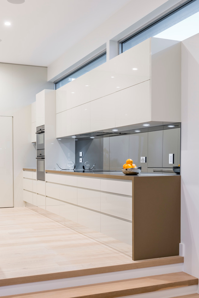 Inspiration for a large contemporary l-shaped eat-in kitchen in Sydney with an undermount sink, recessed-panel cabinets, white cabinets, quartz benchtops, metallic splashback, mirror splashback, stainless steel appliances, light hardwood floors and multiple islands.