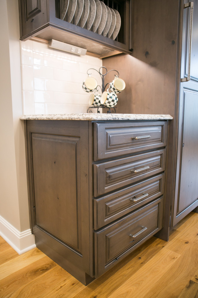 Example of a large transitional u-shaped medium tone wood floor and brown floor kitchen design in Indianapolis with a farmhouse sink, raised-panel cabinets, dark wood cabinets, granite countertops, white backsplash, subway tile backsplash, paneled appliances, an island and multicolored countertops