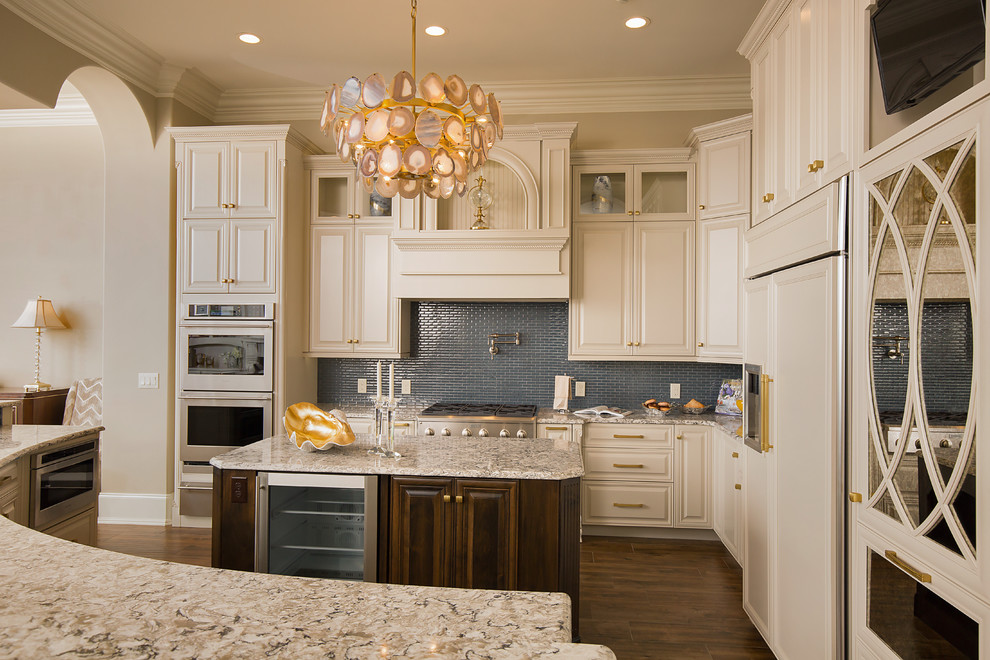 Kitchen - large transitional ceramic tile and brown floor kitchen idea with a farmhouse sink, raised-panel cabinets, beige cabinets, quartz countertops, blue backsplash, glass tile backsplash, stainless steel appliances, an island and beige countertops