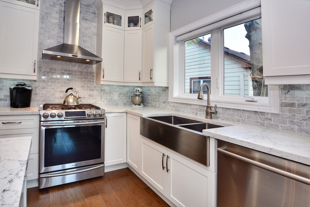 Inspiration for a mid-sized transitional l-shaped medium tone wood floor and brown floor eat-in kitchen remodel in Toronto with a farmhouse sink, shaker cabinets, white cabinets, quartz countertops, gray backsplash, marble backsplash, stainless steel appliances, an island and white countertops