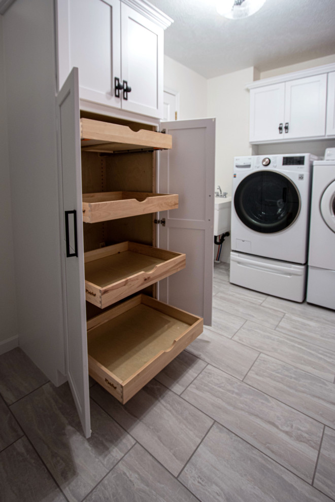 Photo of a small transitional dedicated laundry room in Cleveland with an utility sink, flat-panel cabinets, white cabinets, ceramic floors, a side-by-side washer and dryer and grey floor.