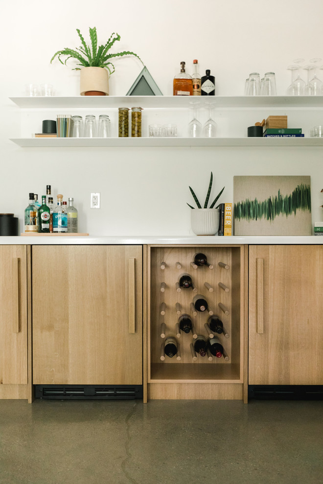 Photo of a mid-sized modern single-wall home bar in Los Angeles with no sink, flat-panel cabinets, light wood cabinets, quartz benchtops, white splashback, concrete floors, grey floor and white benchtop.
