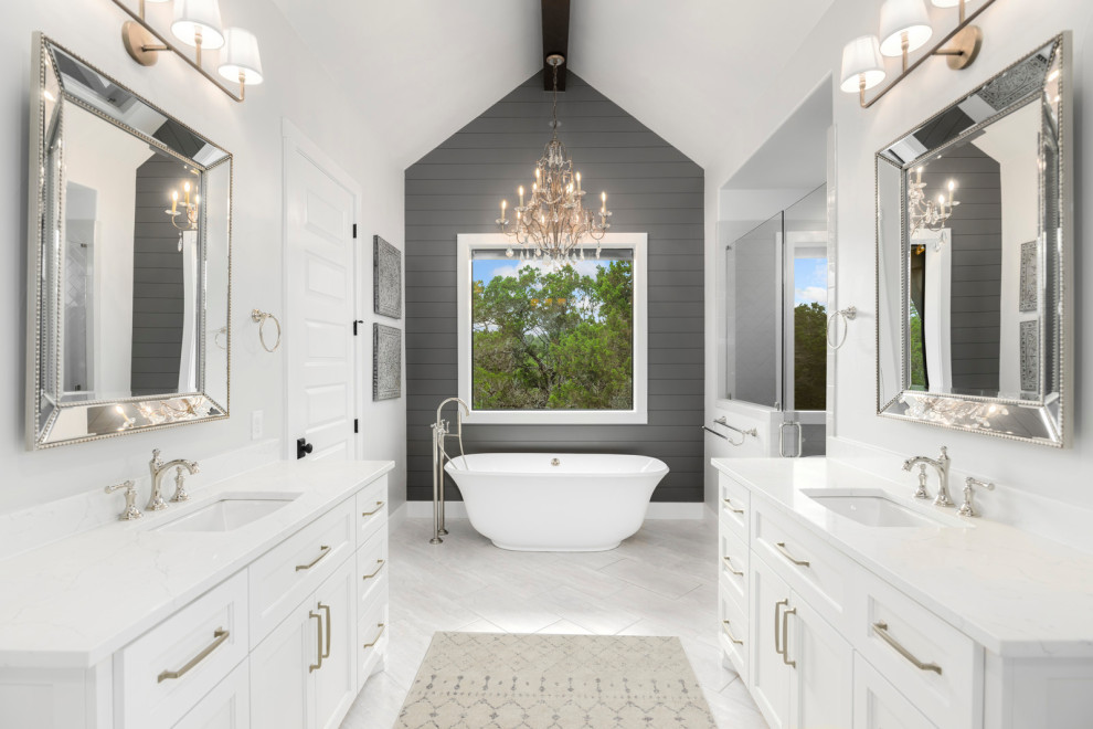 Design ideas for a mid-sized country master bathroom in Austin with raised-panel cabinets, white cabinets, a freestanding tub, an alcove shower, a one-piece toilet, white tile, white walls, porcelain floors, a drop-in sink, marble benchtops, white floor, a hinged shower door, white benchtops, an enclosed toilet, a double vanity, a built-in vanity, vaulted and planked wall panelling.