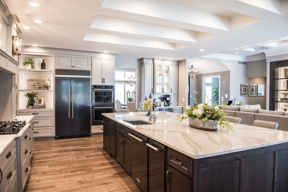 Open concept kitchen - huge transitional l-shaped medium tone wood floor and brown floor open concept kitchen idea with a single-bowl sink, glass-front cabinets, gray cabinets, quartz countertops, gray backsplash, mirror backsplash, stainless steel appliances, an island and white countertops