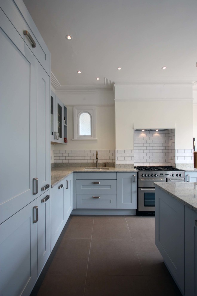 Design ideas for a large traditional l-shaped eat-in kitchen in London with an undermount sink, shaker cabinets, blue cabinets, granite benchtops, ceramic splashback, stainless steel appliances, porcelain floors, with island and white splashback.