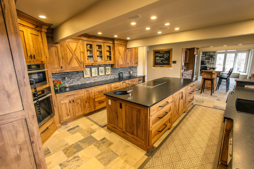 This is an example of a mid-sized country galley eat-in kitchen in Other with granite benchtops, with island, an undermount sink, shaker cabinets, medium wood cabinets, grey splashback, matchstick tile splashback, stainless steel appliances, limestone floors and multi-coloured floor.
