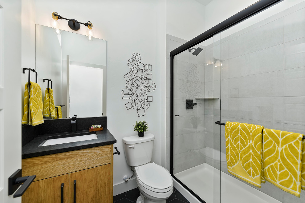 Photo of a transitional kids bathroom in Boise with flat-panel cabinets, medium wood cabinets, an alcove shower, a two-piece toilet, white tile, ceramic tile, white walls, ceramic floors, an undermount sink, granite benchtops, black floor, a sliding shower screen, black benchtops, a single vanity and a built-in vanity.