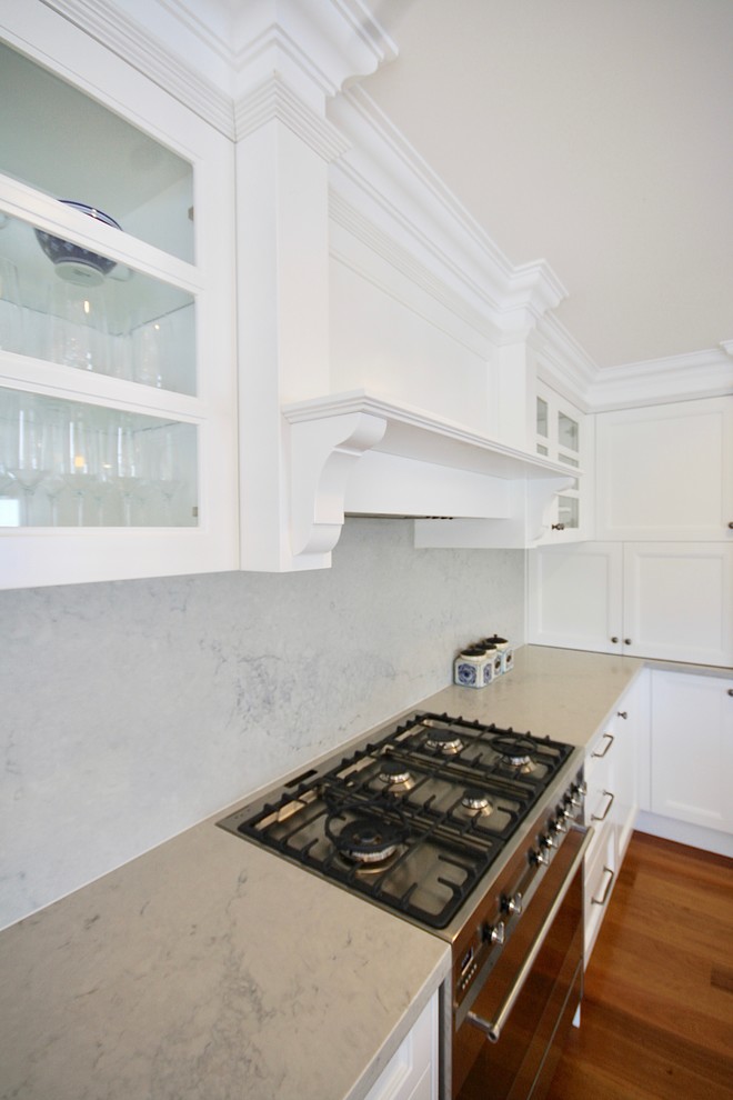 Large transitional l-shaped eat-in kitchen in Sydney with a farmhouse sink, recessed-panel cabinets, white cabinets, quartz benchtops, grey splashback, stone slab splashback, stainless steel appliances, medium hardwood floors, with island and brown floor.