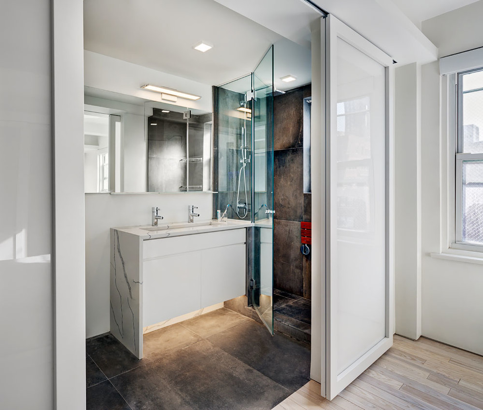 Inspiration for a mid-sized modern bathroom in New York with flat-panel cabinets, white cabinets, an alcove shower, a wall-mount toilet, white walls, an undermount sink, marble benchtops, cement tiles, black tile and cement tile.