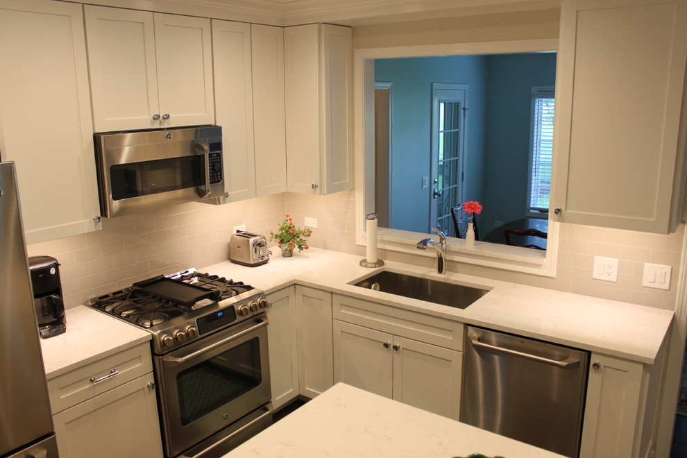 Inspiration for a mid-sized transitional l-shaped dark wood floor and brown floor enclosed kitchen remodel in Chicago with an undermount sink, recessed-panel cabinets, white cabinets, quartzite countertops, white backsplash, subway tile backsplash, stainless steel appliances and an island