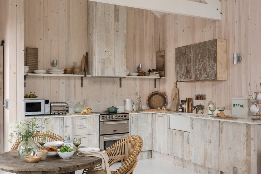 Inspiration for a mid-sized country l-shaped eat-in kitchen in Cornwall with a farmhouse sink, flat-panel cabinets, beige cabinets, beige splashback, timber splashback, stainless steel appliances, no island, grey floor and white benchtop.