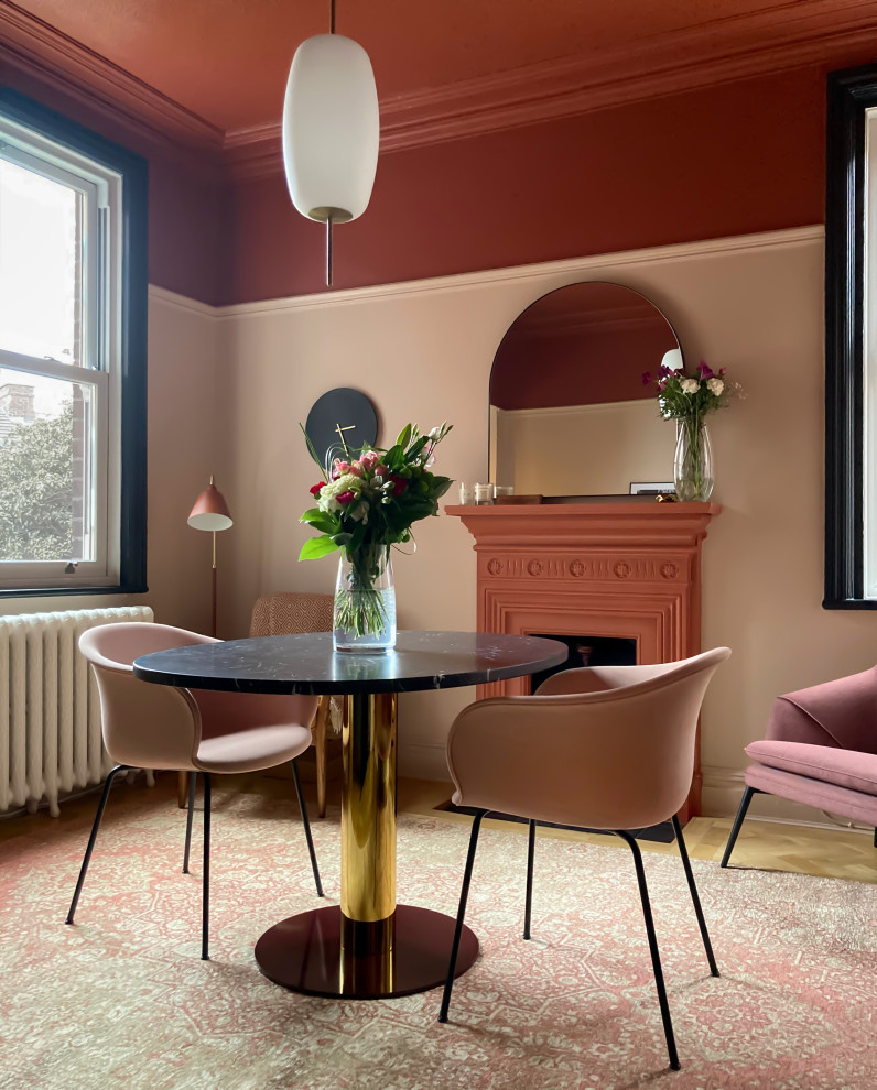 This is an example of a mid-sized eclectic kitchen/dining combo in Manchester with pink walls, medium hardwood floors, a standard fireplace, a metal fireplace surround, beige floor and wallpaper.