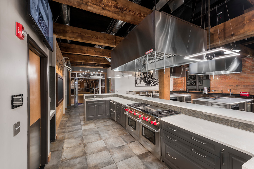 Expansive industrial u-shaped eat-in kitchen in New York with an undermount sink, raised-panel cabinets, grey cabinets, quartz benchtops, grey splashback, glass tile splashback, stainless steel appliances, ceramic floors, multiple islands, beige floor and white benchtop.