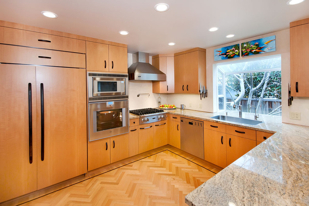 Design ideas for a mid-sized modern u-shaped open plan kitchen in San Francisco with a single-bowl sink, flat-panel cabinets, light wood cabinets, granite benchtops, beige splashback, stainless steel appliances and medium hardwood floors.
