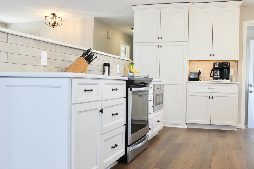 他の地域にある中くらいなトランジショナルスタイルのおしゃれなキッチン (アンダーカウンターシンク、フラットパネル扉のキャビネット、白いキャビネット、クオーツストーンカウンター、ベージュキッチンパネル、セラミックタイルのキッチンパネル、シルバーの調理設備、クッションフロア、茶色い床、白いキッチンカウンター) の写真