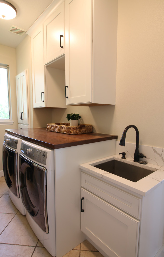 This is an example of a small country galley dedicated laundry room in Denver with a single-bowl sink, flat-panel cabinets, white cabinets, wood benchtops, white splashback, engineered quartz splashback, beige walls, ceramic floors, a side-by-side washer and dryer, beige floor and brown benchtop.