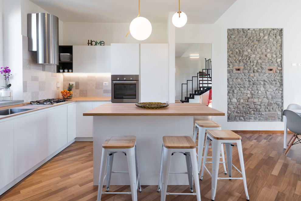 Photo of a contemporary l-shaped kitchen in Florence with a drop-in sink, flat-panel cabinets, white cabinets, wood benchtops, grey splashback, stainless steel appliances, medium hardwood floors, with island, brown floor and brown benchtop.