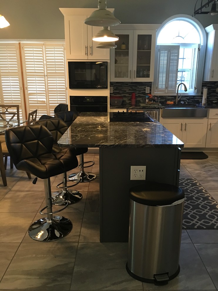 Mid-sized contemporary l-shaped kitchen pantry in Atlanta with a farmhouse sink, shaker cabinets, white cabinets, granite benchtops, multi-coloured splashback, stainless steel appliances, ceramic floors, with island and mosaic tile splashback.