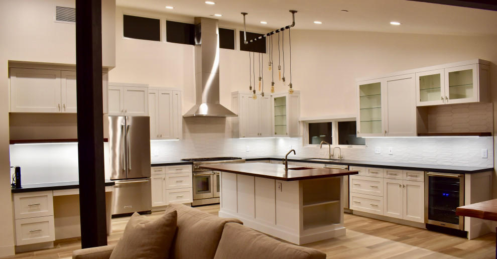 Inspiration for a large transitional l-shaped porcelain tile and brown floor eat-in kitchen remodel with an undermount sink, shaker cabinets, white cabinets, quartz countertops, white backsplash, ceramic backsplash, stainless steel appliances, an island and black countertops