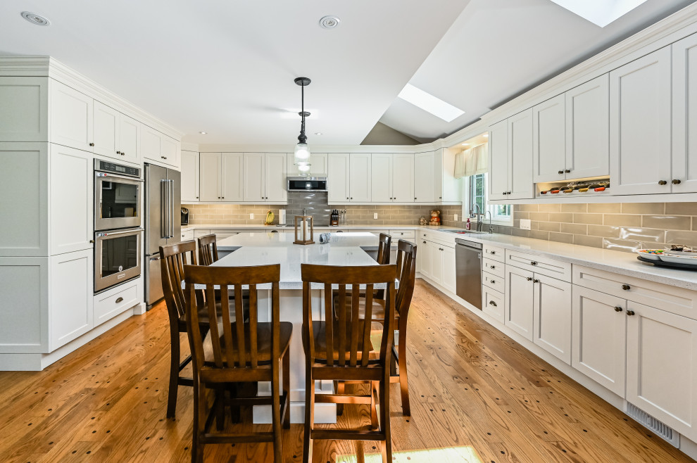 Kitchen - transitional u-shaped medium tone wood floor and brown floor kitchen idea with an undermount sink, shaker cabinets, white cabinets, gray backsplash, subway tile backsplash, an island and white countertops