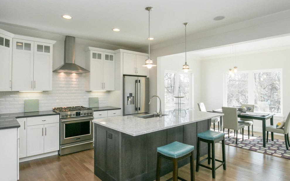 Mid-sized transitional l-shaped medium tone wood floor and brown floor eat-in kitchen photo in Cedar Rapids with an undermount sink, shaker cabinets, white cabinets, marble countertops, white backsplash, subway tile backsplash, stainless steel appliances and an island