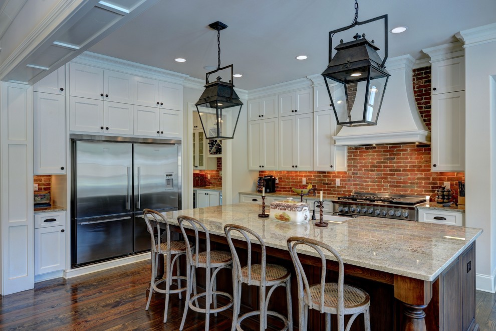 This is an example of a country l-shaped kitchen in Atlanta with a farmhouse sink, shaker cabinets, white cabinets, granite benchtops, brick splashback, stainless steel appliances, dark hardwood floors, with island, red splashback, brown floor and grey benchtop.