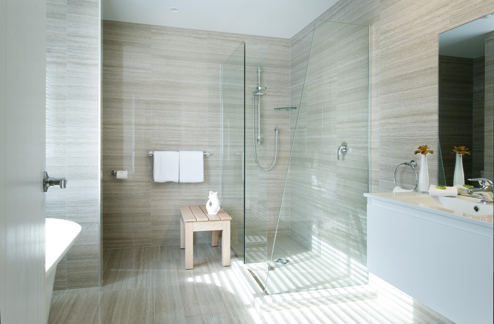 Mid-sized contemporary bathroom in Auckland with white cabinets, a freestanding tub, a wall-mount toilet, beige tile, ceramic tile, beige walls, ceramic floors, an integrated sink and engineered quartz benchtops.