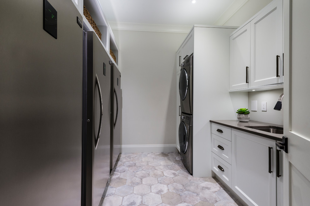 Design ideas for an expansive traditional u-shaped laundry room in Vancouver with a farmhouse sink, recessed-panel cabinets, white cabinets, granite benchtops, grey splashback, porcelain splashback, medium hardwood floors and brown floor.