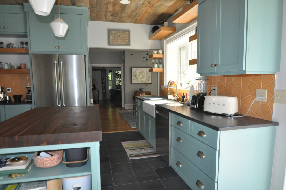 Photo of a mid-sized transitional kitchen in Boston with a farmhouse sink, shaker cabinets, blue cabinets, quartz benchtops, orange splashback, porcelain splashback, stainless steel appliances, slate floors, with island, black floor, black benchtop and wood.