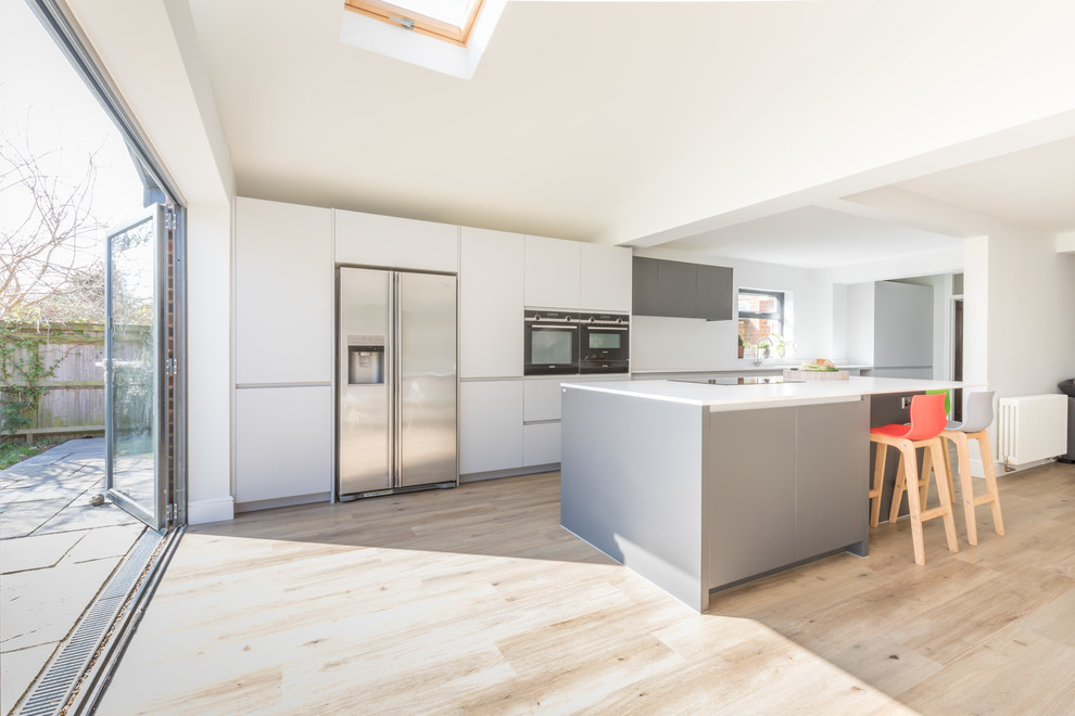 Inspiration for a mid-sized contemporary galley open plan kitchen in Sussex with an integrated sink, flat-panel cabinets, grey cabinets, solid surface benchtops, stainless steel appliances, with island and white benchtop.