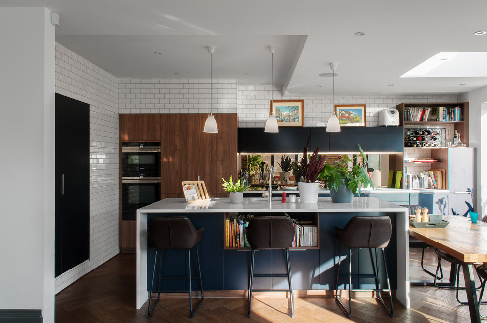 Design ideas for a mid-sized contemporary l-shaped open plan kitchen in London with flat-panel cabinets, solid surface benchtops, medium hardwood floors, with island, white benchtop, an undermount sink, medium wood cabinets, brown floor and mirror splashback.