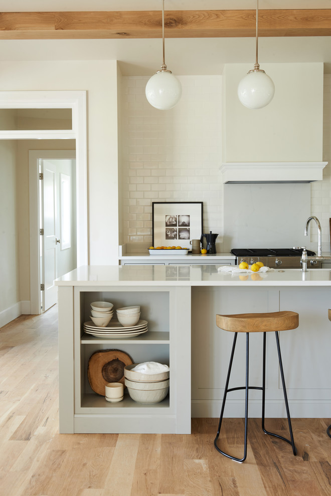Example of a mid-sized transitional l-shaped light wood floor and brown floor open concept kitchen design with white backsplash, subway tile backsplash, stainless steel appliances and an island