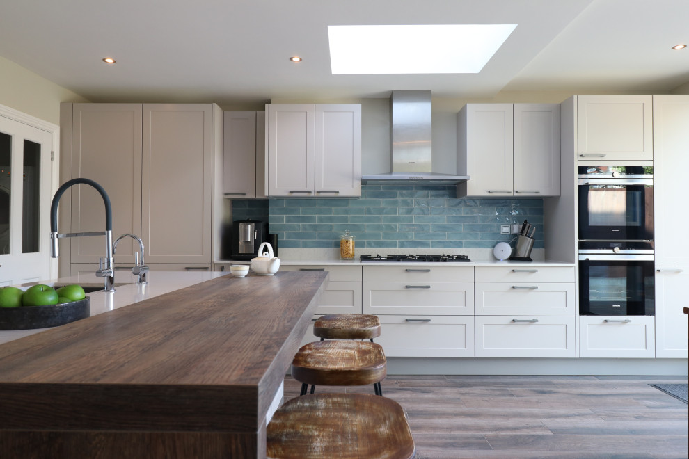 Design ideas for a large transitional l-shaped eat-in kitchen in London with a drop-in sink, shaker cabinets, quartzite benchtops, ceramic splashback, panelled appliances, with island, white benchtop, white cabinets, blue splashback, medium hardwood floors and brown floor.