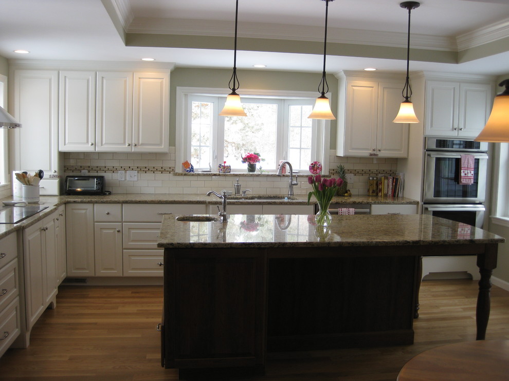 Transitional u-shaped medium tone wood floor eat-in kitchen photo in Boston with an undermount sink, raised-panel cabinets, white cabinets, granite countertops, white backsplash, ceramic backsplash, stainless steel appliances, an island and beige countertops
