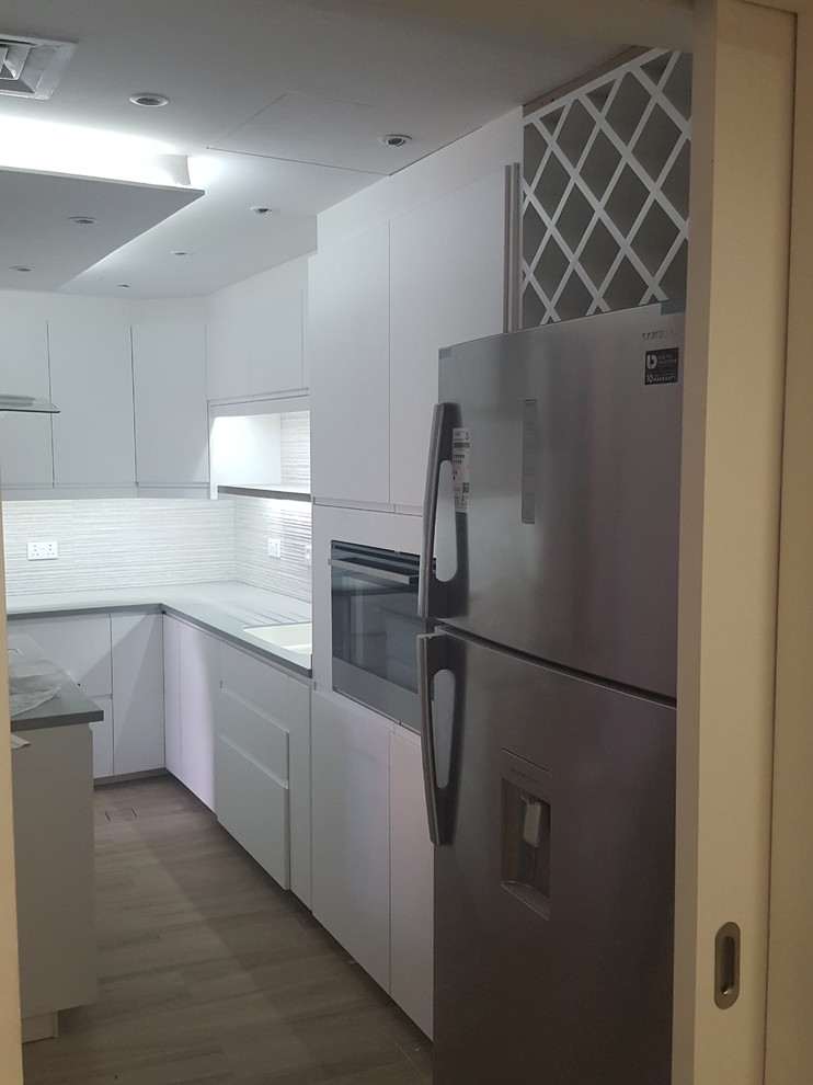 Example of a large minimalist l-shaped ceramic tile kitchen pantry design with an integrated sink, flat-panel cabinets, white cabinets, ceramic backsplash, black appliances and an island