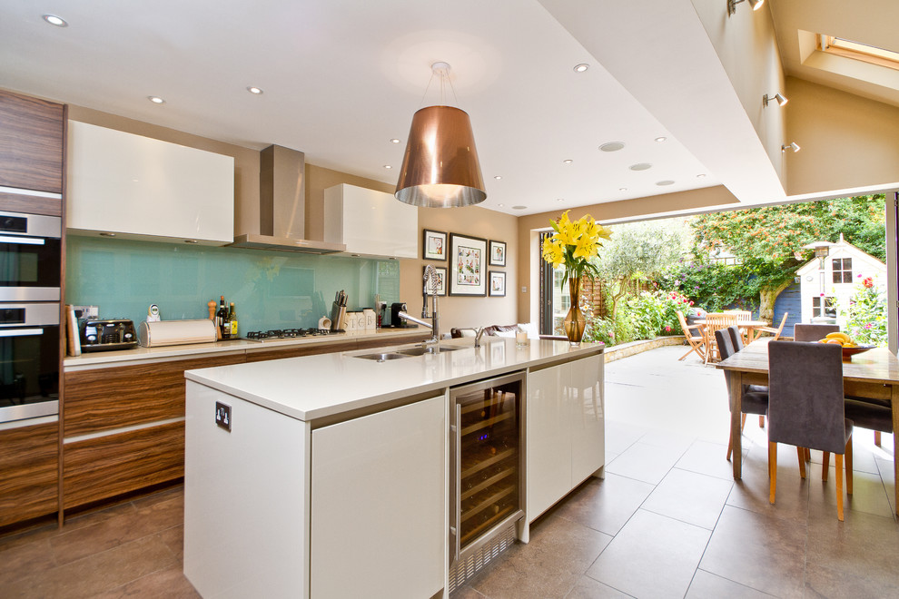 This is an example of a contemporary eat-in kitchen in London with stainless steel appliances, a double-bowl sink, flat-panel cabinets, dark wood cabinets and glass sheet splashback.