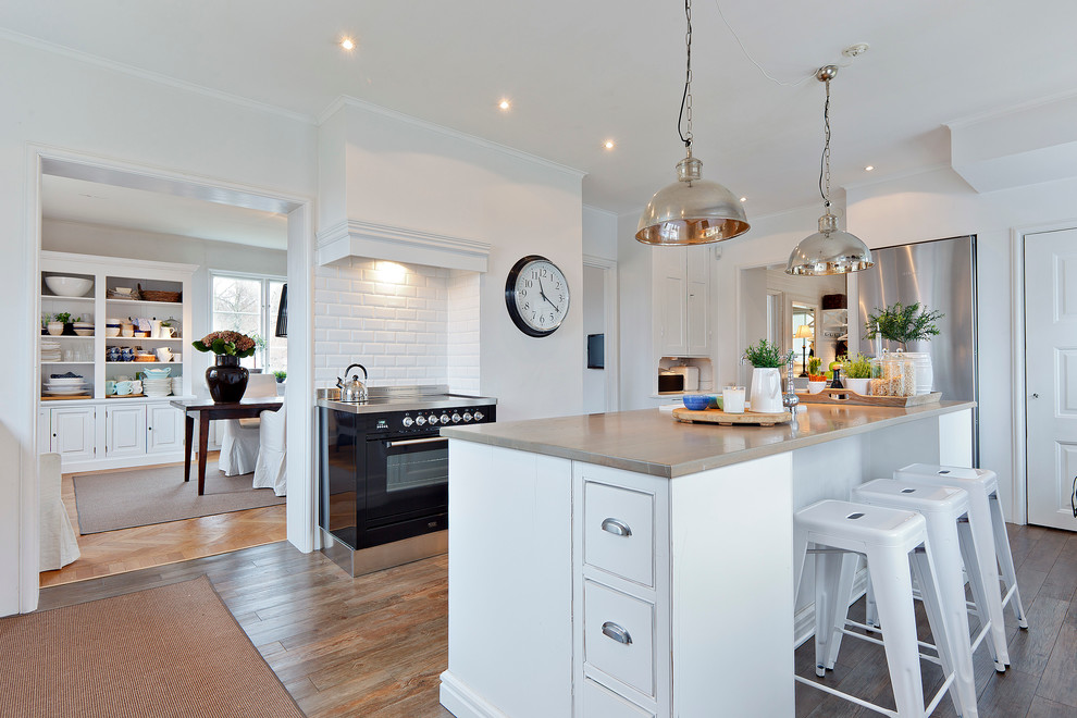 This is an example of a large transitional single-wall kitchen in Stockholm with with island, raised-panel cabinets, white cabinets, wood benchtops and medium hardwood floors.