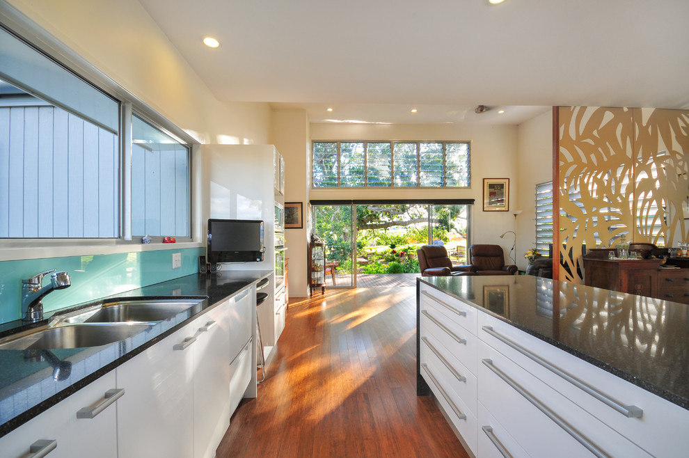 Inspiration for a mid-sized contemporary galley open plan kitchen in Brisbane with an undermount sink, quartz benchtops, green splashback, glass sheet splashback, stainless steel appliances, bamboo floors and with island.