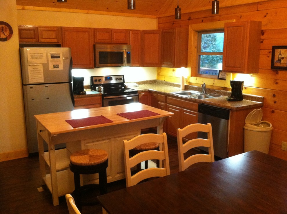 Example of a mountain style l-shaped dark wood floor eat-in kitchen design with a drop-in sink, light wood cabinets, laminate countertops, stainless steel appliances and an island