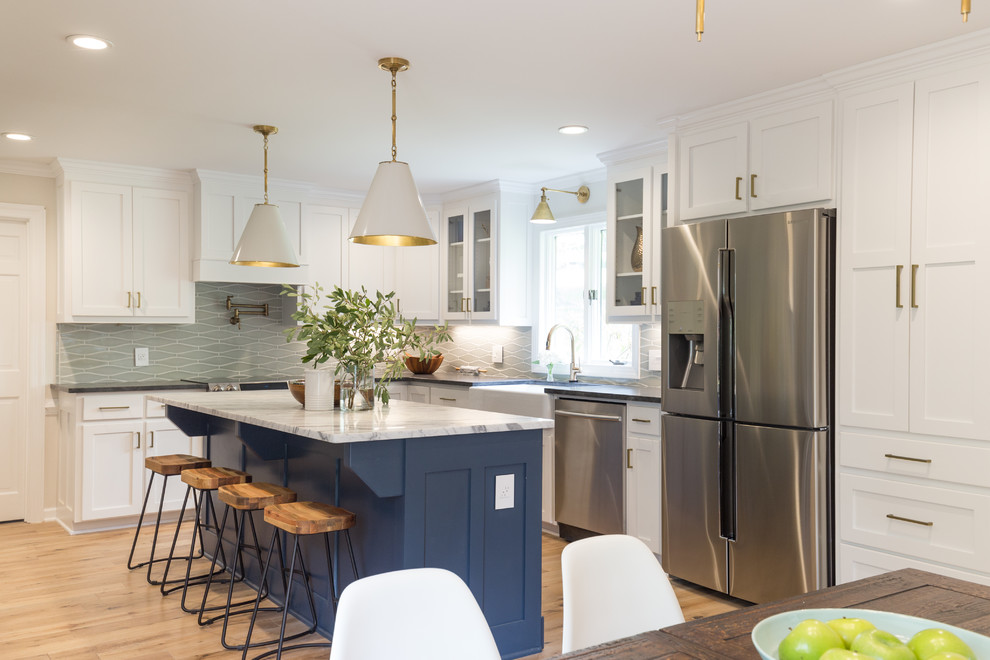 Eat-in kitchen - transitional l-shaped light wood floor and brown floor eat-in kitchen idea with white cabinets, gray backsplash, ceramic backsplash, an island, a farmhouse sink, shaker cabinets and stainless steel appliances