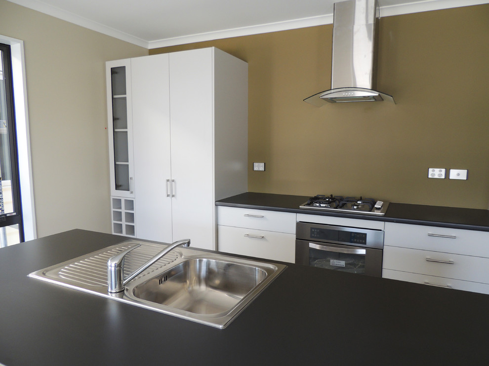 Mid-sized modern galley open plan kitchen in Christchurch with a drop-in sink, flat-panel cabinets, grey cabinets, laminate benchtops, glass sheet splashback, stainless steel appliances, vinyl floors and with island.