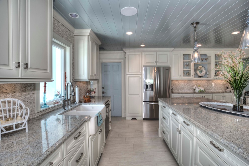 Photo of a large transitional u-shaped eat-in kitchen in Tampa with a farmhouse sink, raised-panel cabinets, white cabinets, granite benchtops, beige splashback, stone tile splashback, stainless steel appliances, porcelain floors and with island.
