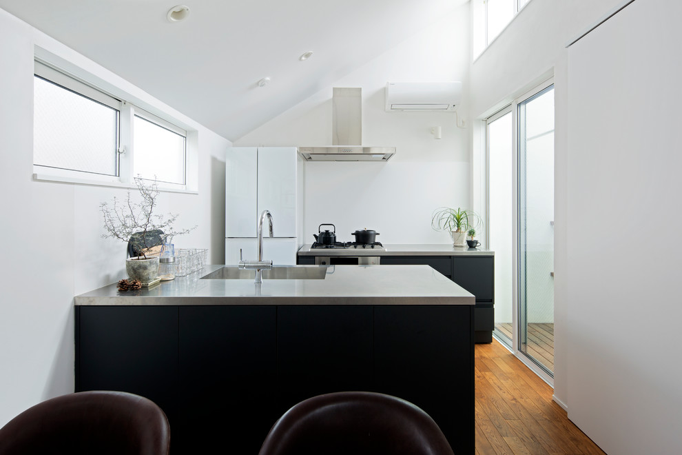 This is an example of a contemporary galley kitchen in Tokyo with an integrated sink, stainless steel benchtops, blue splashback, black appliances, medium hardwood floors, with island, brown floor and blue benchtop.