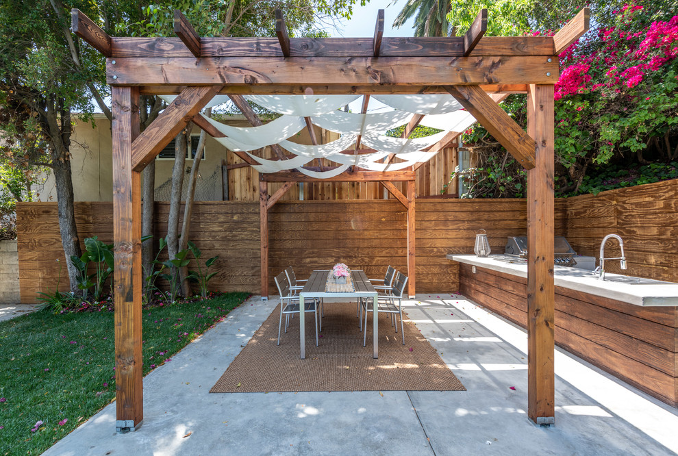This is an example of a mid-sized contemporary backyard deck in Los Angeles with an outdoor kitchen and a pergola.