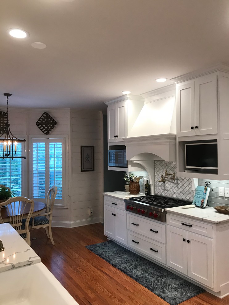 Inspiration for a mid-sized transitional u-shaped medium tone wood floor and brown floor eat-in kitchen remodel in Atlanta with a farmhouse sink, shaker cabinets, white cabinets, subway tile backsplash, stainless steel appliances, an island and granite countertops